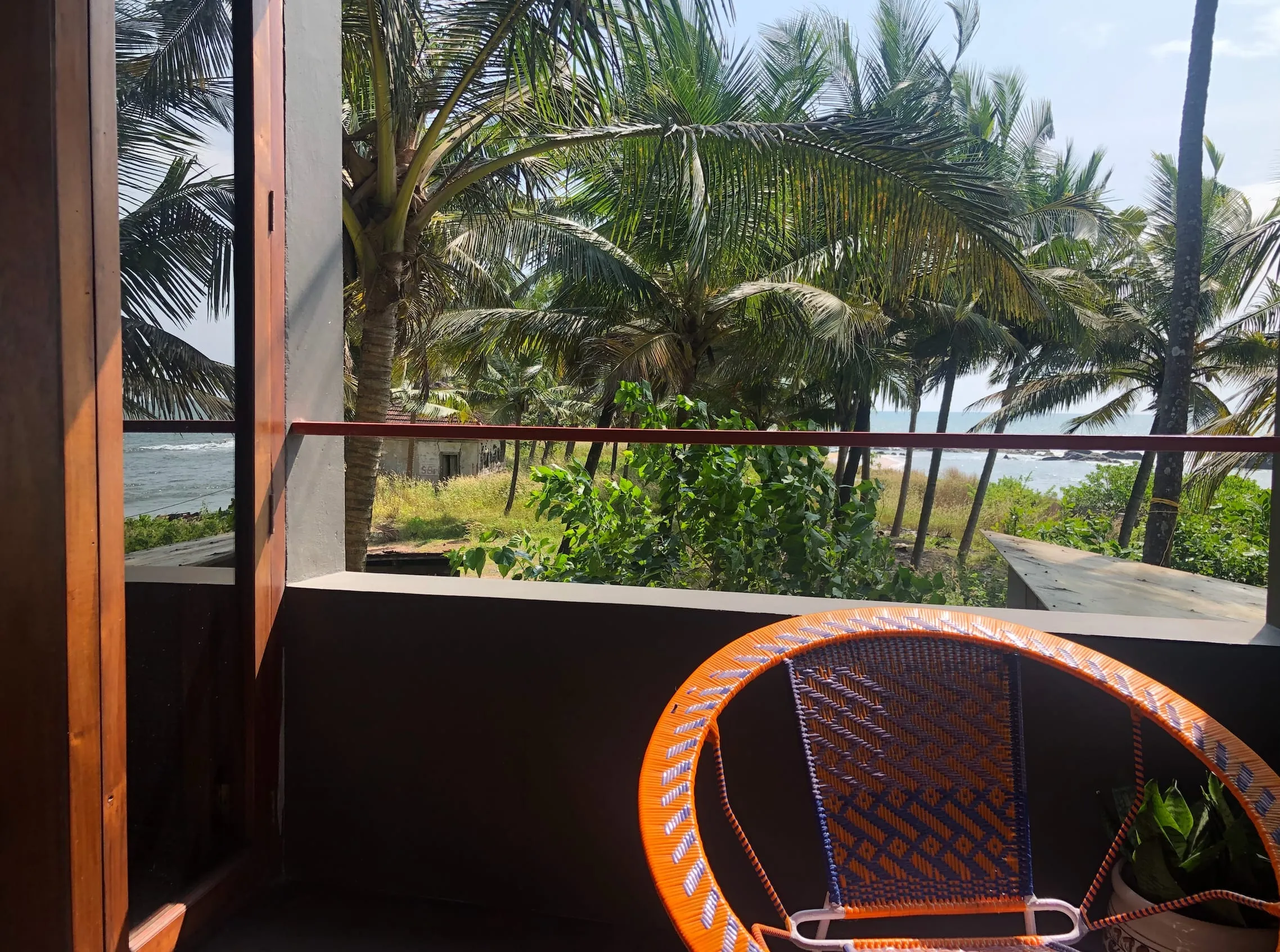 The sea beyond the palm trees, seen from the balcony of our beach house in Kannur, with an orange woven chair in front