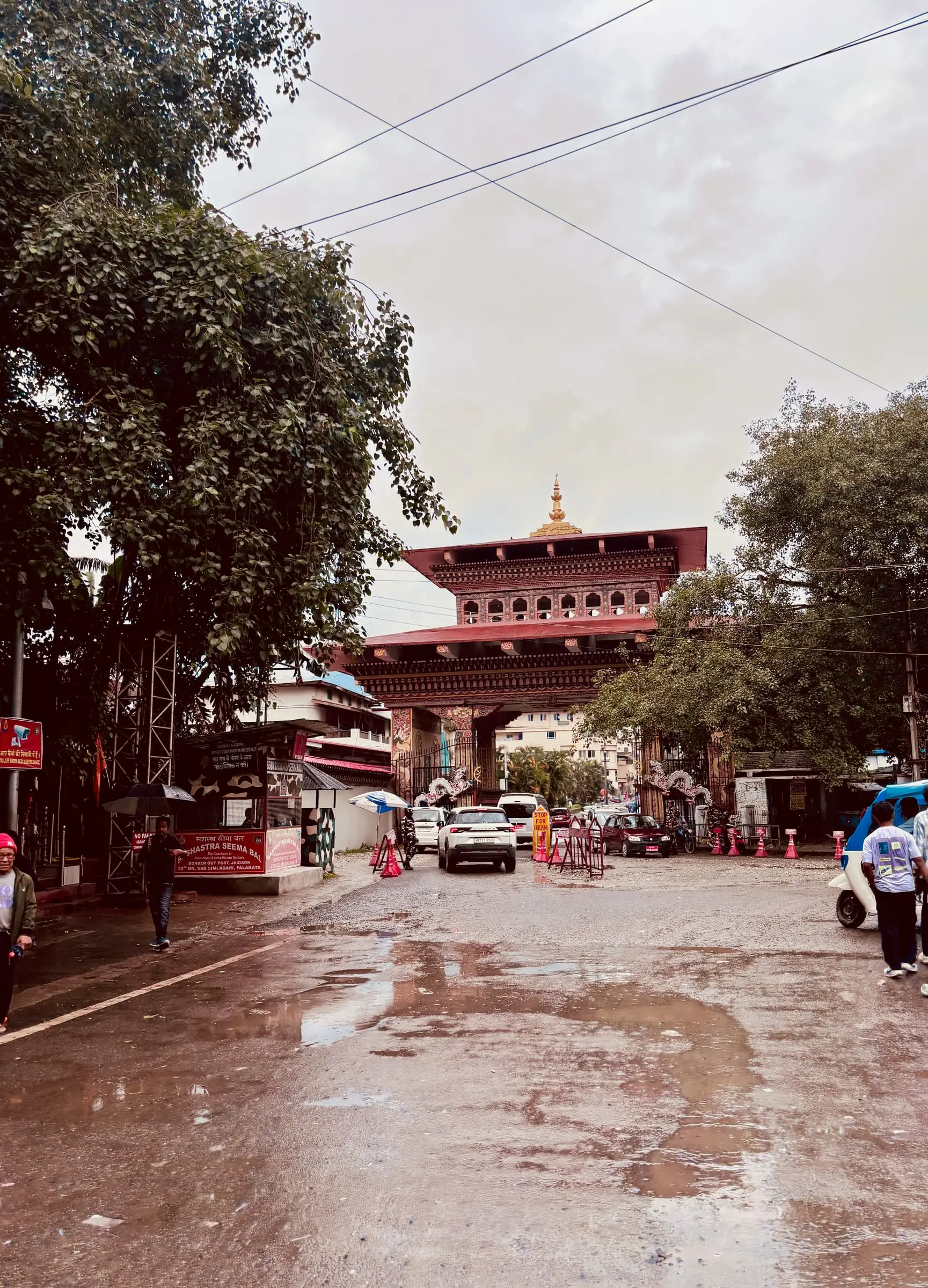The Bhutan Gate at Phuentsholing seen from the Jaigaon side on a wet morning, cars at the border and the Indian border post on the left