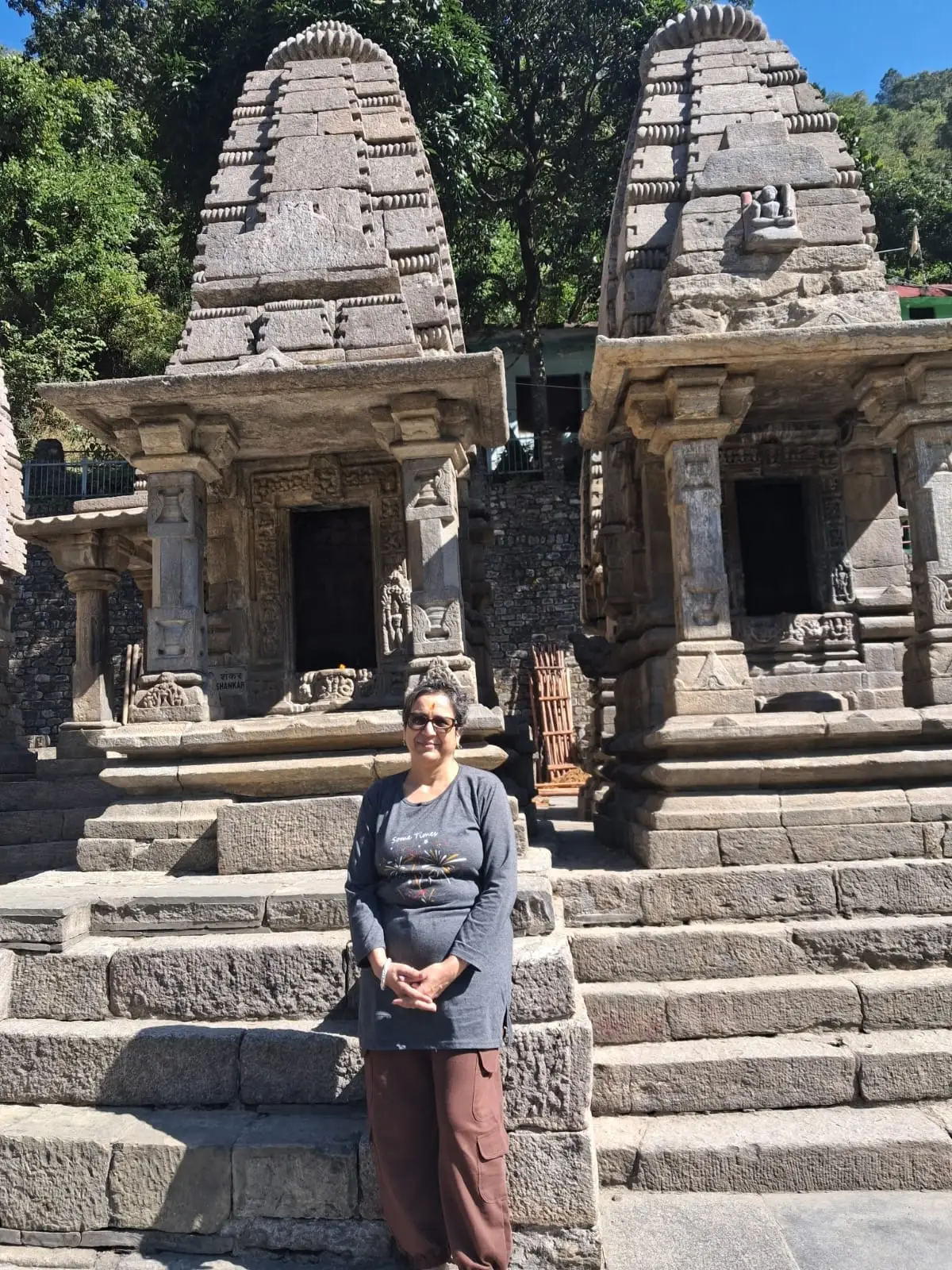 Jhumka before two stone temples with tall carved spires at Adi Badri