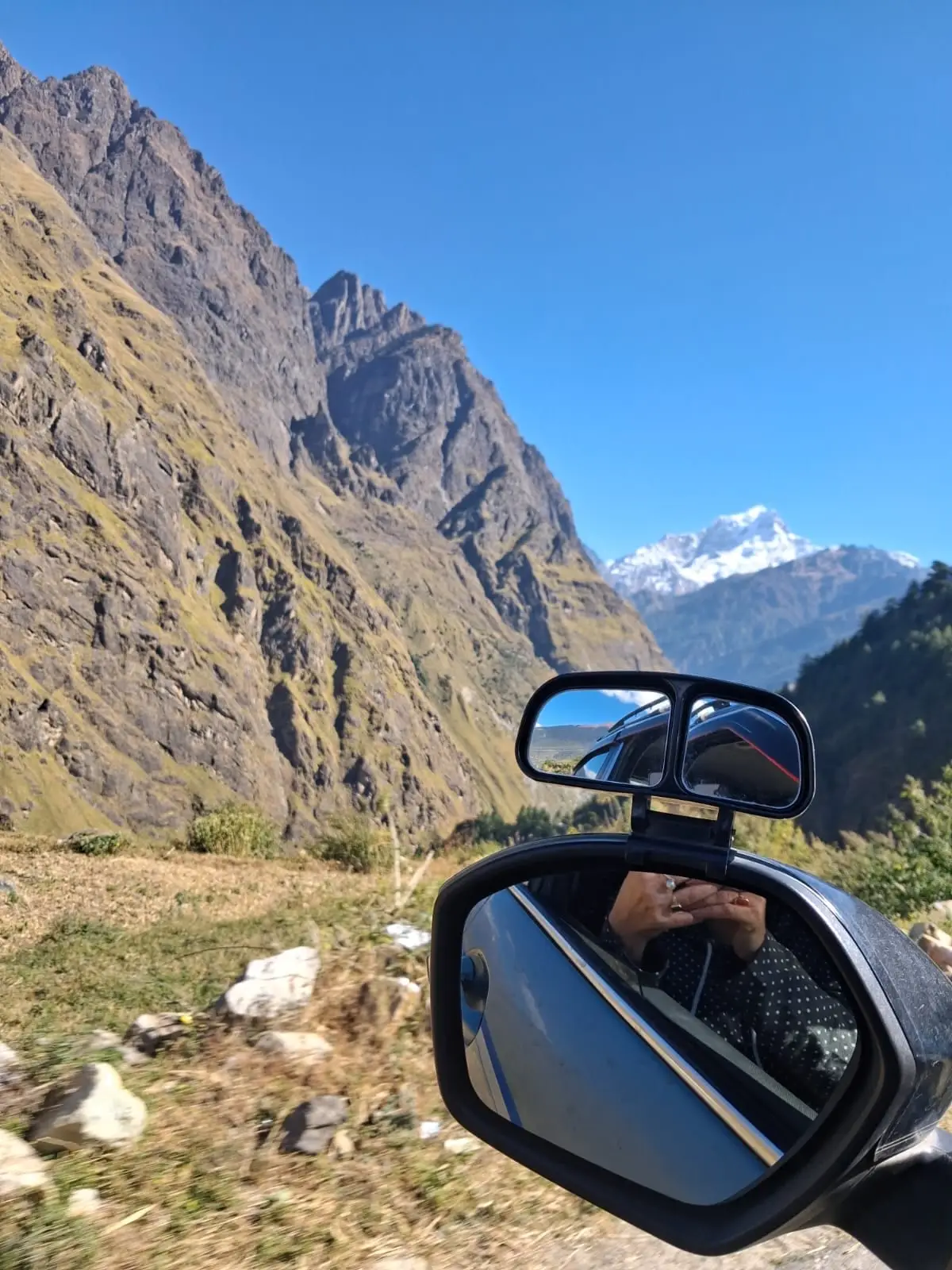 A valley and a snow peak beyond it, seen past the car's side mirror