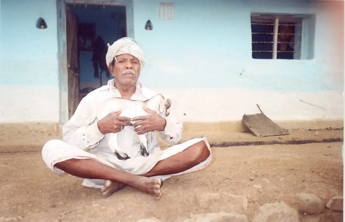 Dhandekar, one of the oldest men in the Korku community, sitting outside his house in Melghat with a goat, 2009
