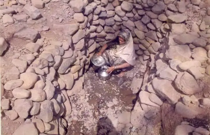 The difficult everyday struggle of an Adivasi woman seeking basic amenities: she fills a pot at the bottom of a stone-lined well