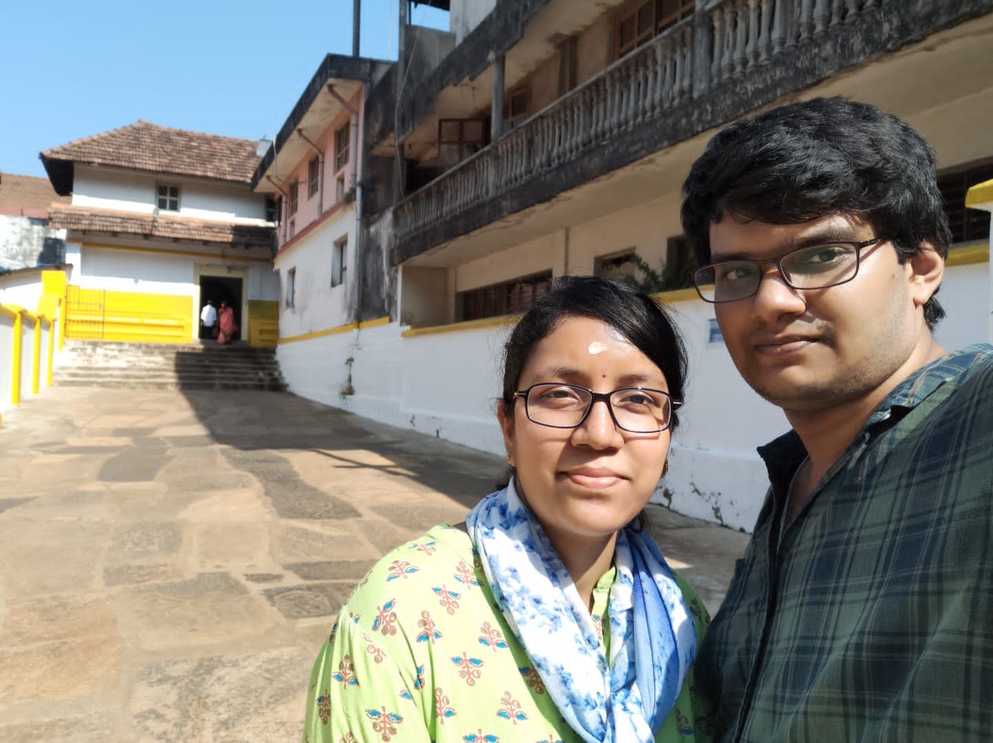 Two visitors take a selfie in the stone courtyard at Kukke Subramanya
